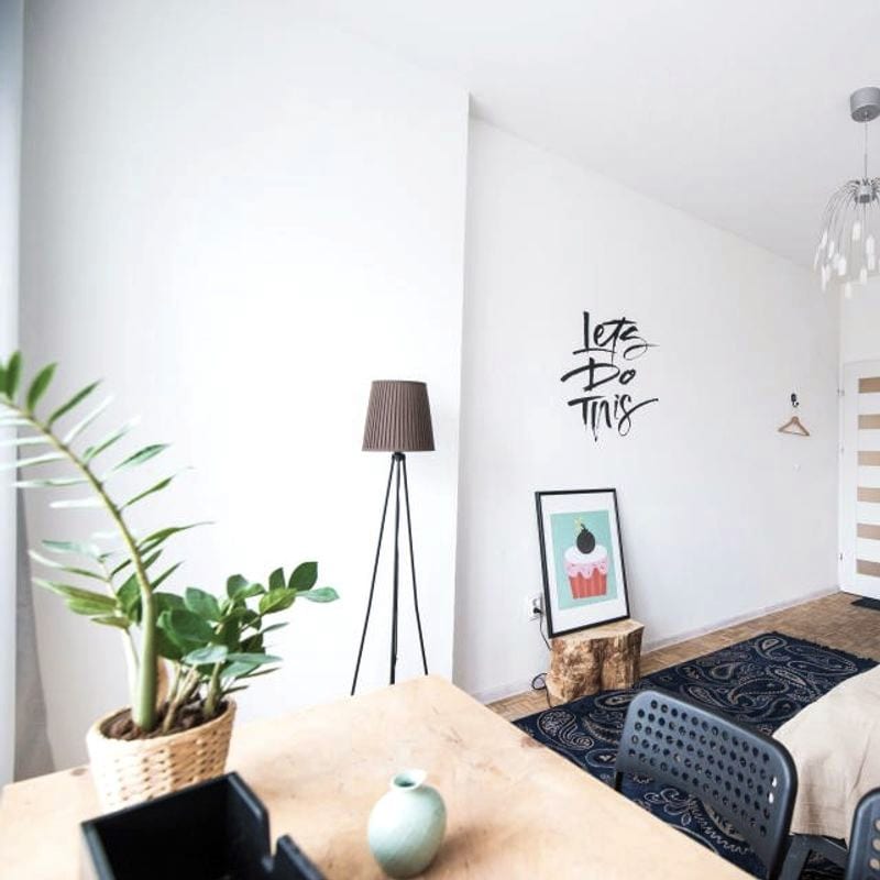 Dormitorio luminoso con la cama hecha, una lámpara de pie y una planta